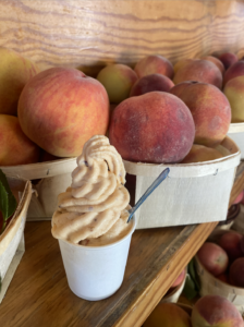 Quarry Cones Real Fruit Ice Cream in a cup sitting in front of ripe peaches